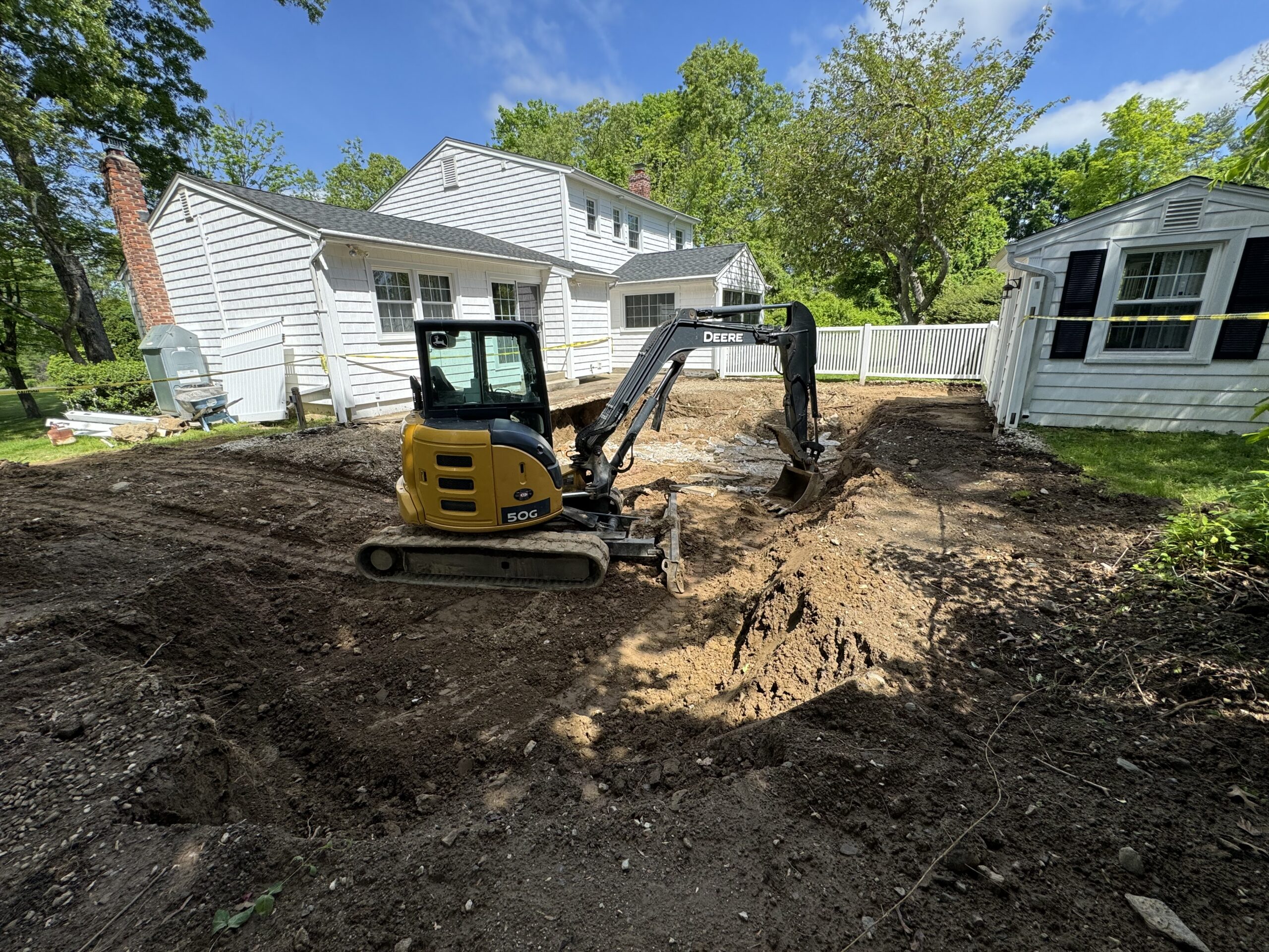 yellow excavator in a backyard in a hole where swimming pool was removed