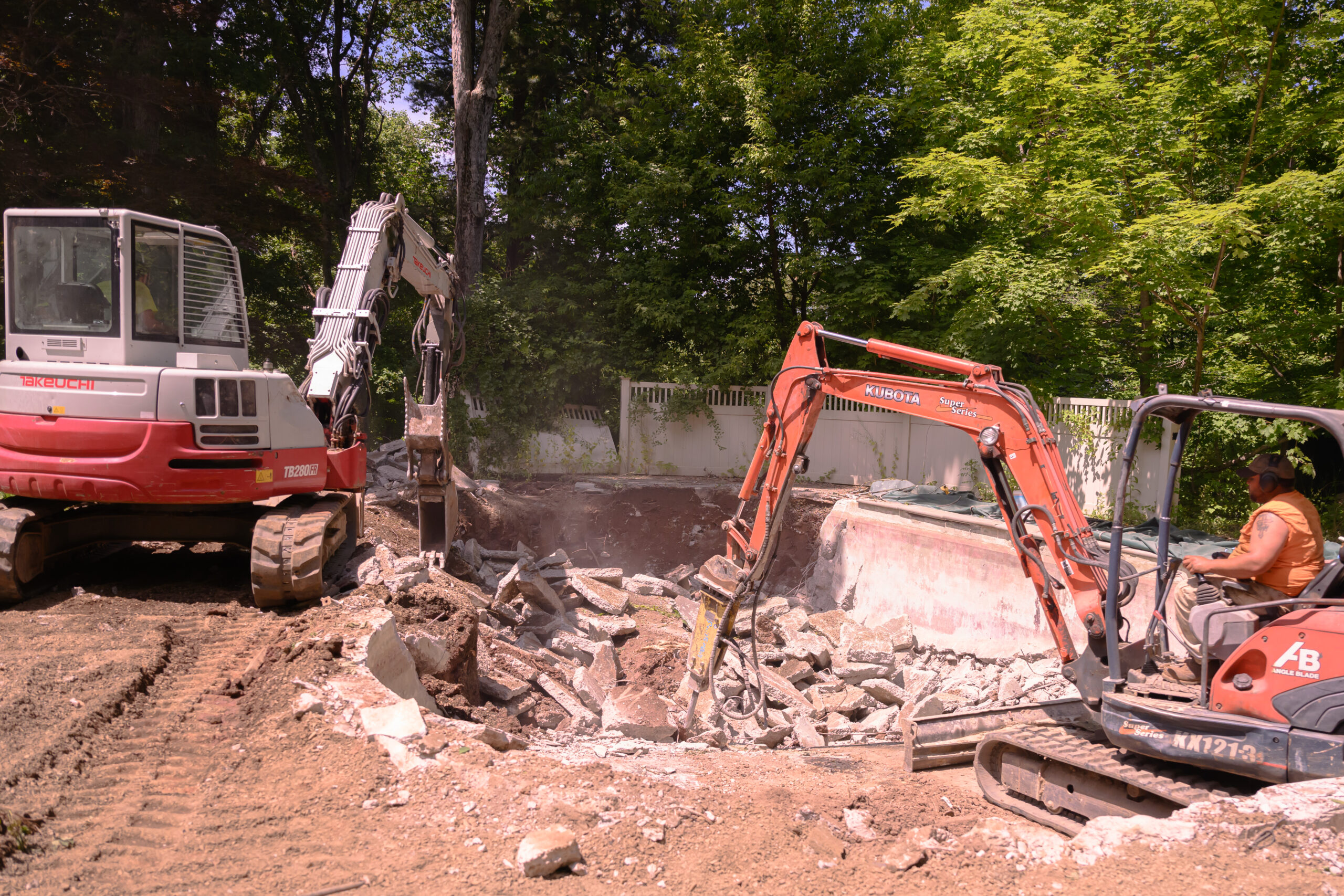 A red and orange excavator diligently working on pool demolition, showcasing the construction process.