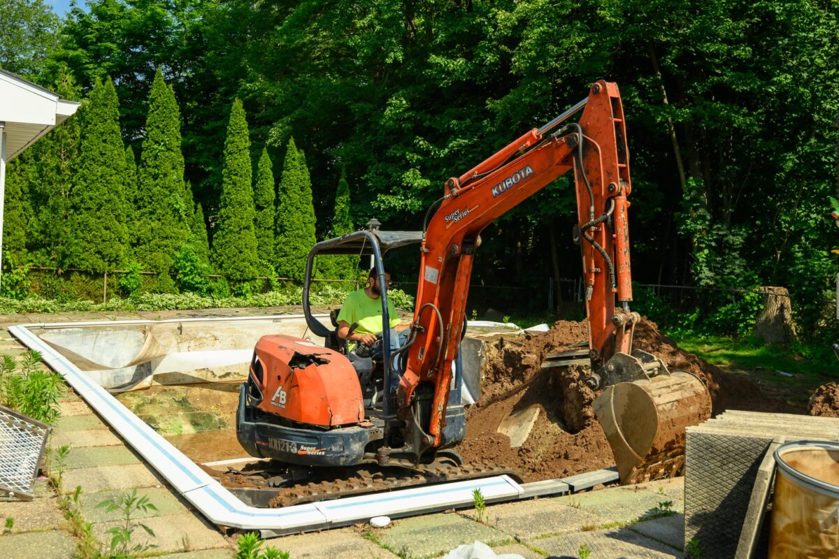 A small excavator loosening concrete frame of pool. Pool removal Bristol CT