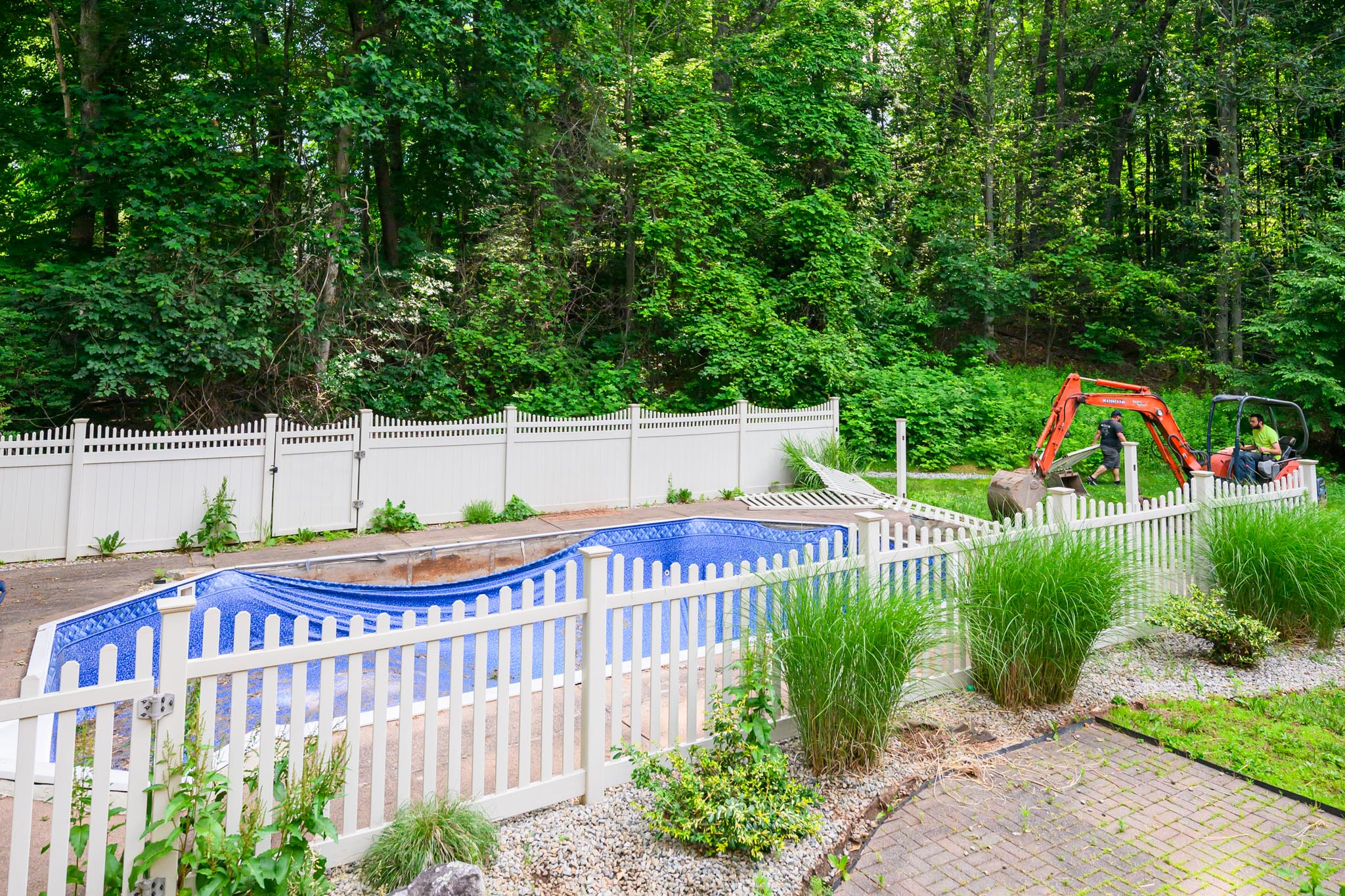 A Blue tarped swimming pool surrounded by a white fence.