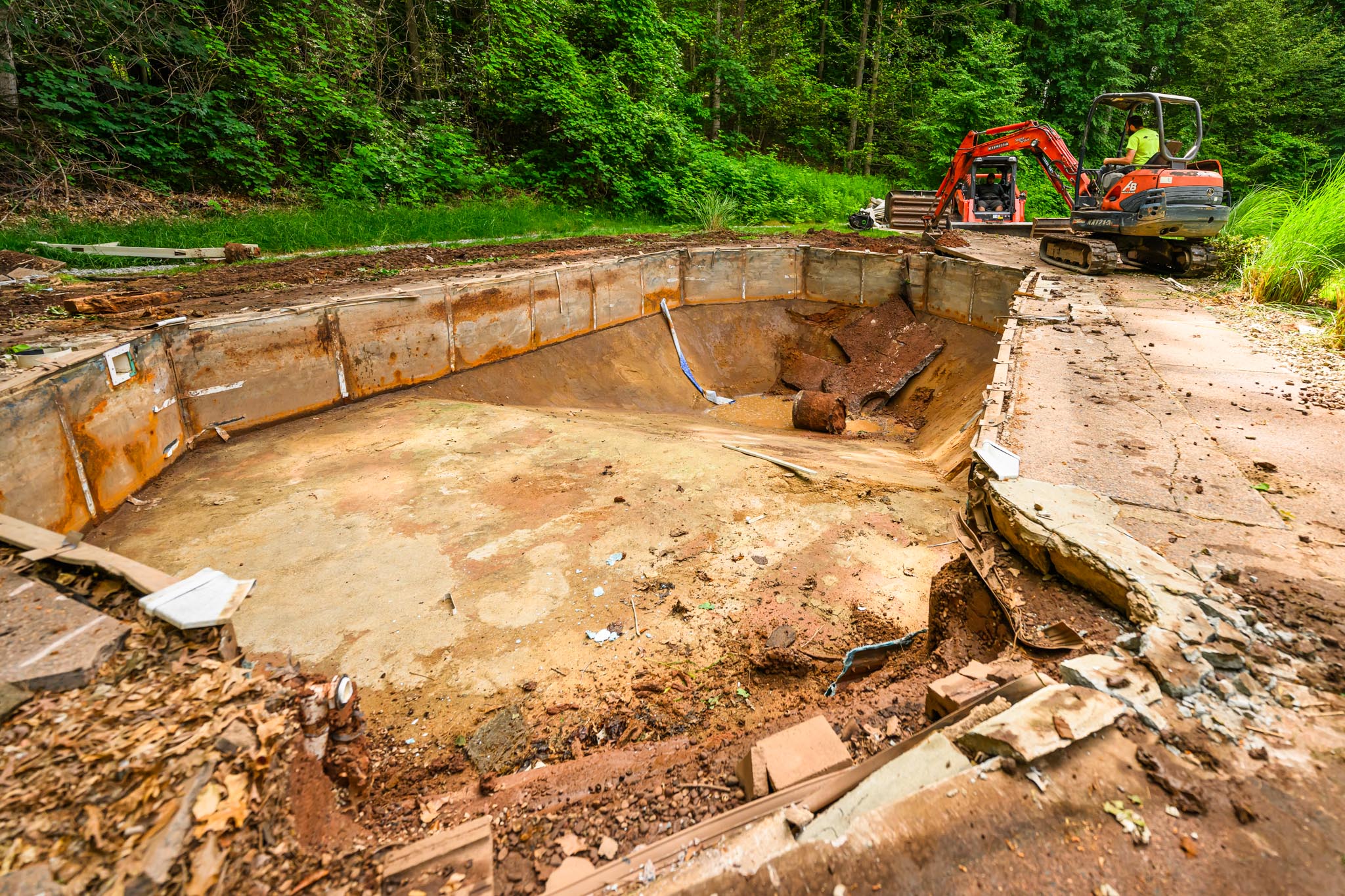 Cement in ground pool in a large backyard covered in debris.