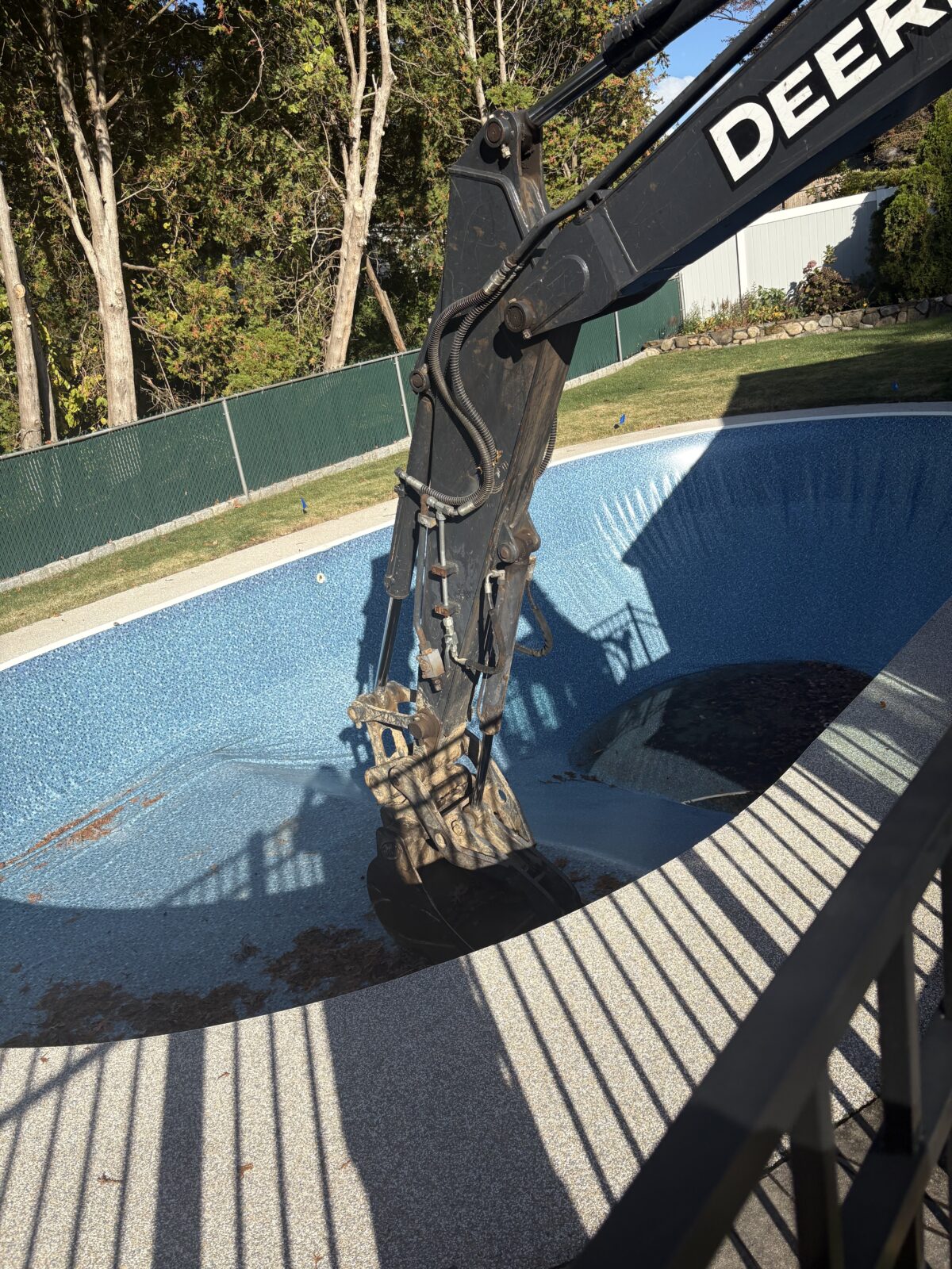 Excavator bucket inside a drained vinyl liner inground pool in Stratford CT, beginning the demolition and removal process